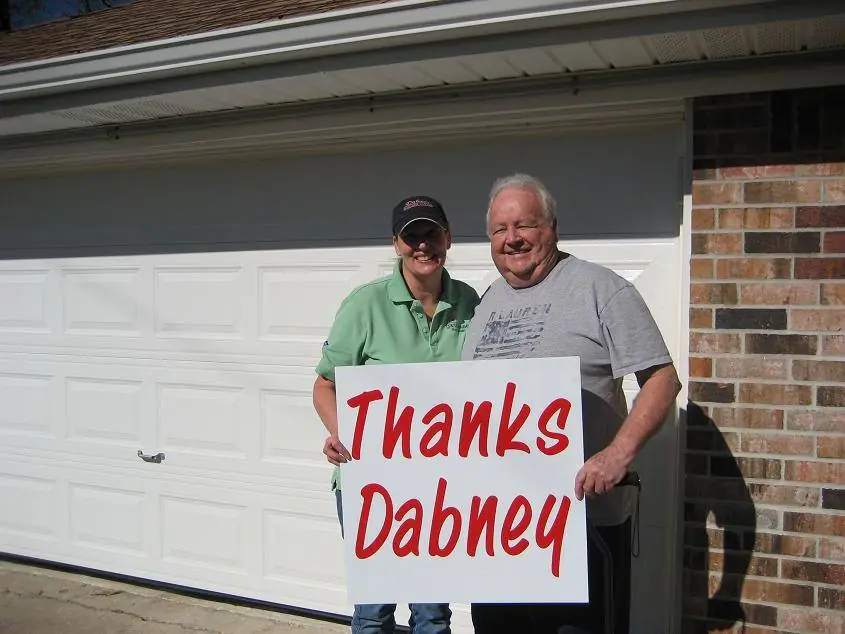 A Dabney customer and a Dabney team member with a thank you sign in front of a finished residential garage door