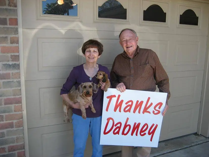 An elderly couple with their pets holding a thank you sign in front of an installed residential garage door